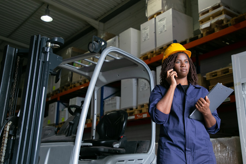 imagen de una operario de logística, con casco, en un almacén cargando una caja.